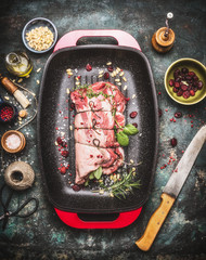 Raw Meat roast preparation in  roaster pan with cooking ingredients and seasoning on dark rustic...