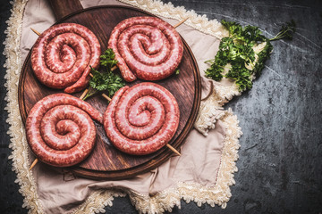 Raw spiral sausages on wooden cutting board, top view, place for text