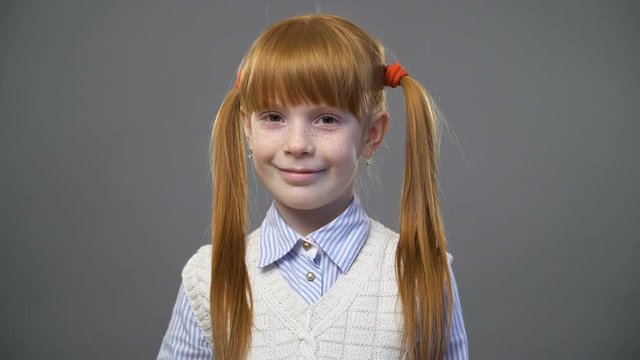 Cute ginger girl with two pigtails looking onto the camera and smiling against gray background
