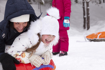 Obraz premium Happy mother and daughter laughing and rolling with snow hill.