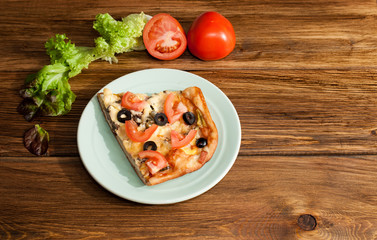 Italian pizza with mushrooms, ham and vegetables on a plate on a wooden, dark background.