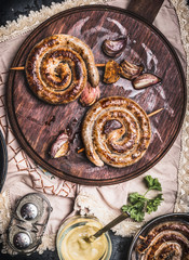 Grilled sausages spiral served on rustic round cutting board with mustard , top view, Country dark style
