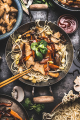 Asian dish with chicken vegetables noodles stir-fry in little wok with chopstick and cooking...