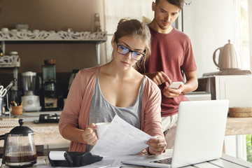 Young family facing financial troubles. Woman in glasses reading information in piece of paper with...