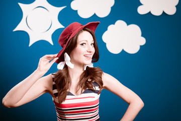 Happy smiling pretty young woman in red hat over blue paper sky with white clouds