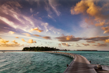 Wooden jetty towards a small island in Maldives at sunset