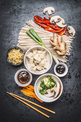 Various Asian vegetarian cooking ingredients and chopsticks with tofu, noodles, ginger, cut vegetables, Sprout,green onion ,hoisin and austern sauce on dark rustic background, top view