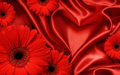 Red satin fabric draped in the form of heart and red gerbera flo