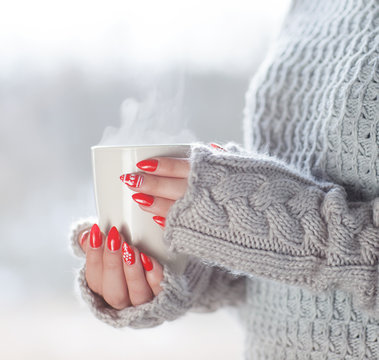 Woman wearing knitted sweater and gloves holding a cup of hot steaming coffee, humorous home heating energy saving