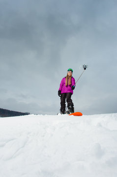 Young woman with the snowboard shooting a selfie by her cell phone 