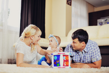 Obraz na płótnie Canvas Мама и папа играют со своей маленькой дочерью и улыбаются друг другу