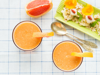 Fresh orange smoothie with grapefruit juice, banana, oatmeal flakes and tofu cheese in glasses on checkered table cloth. Top view
