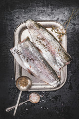 Raw trout fish fillet with fennel seeds and salt on dark rustic background, top view