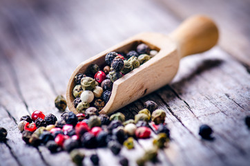 Mixed whole pepper on a wooden scoop. Natural old background. Concept of food, spice