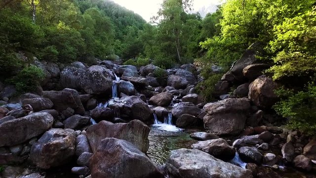 volo radente sopra l'acqua e le rocce del torrente con acque frizzanti, piante verdi e rapide