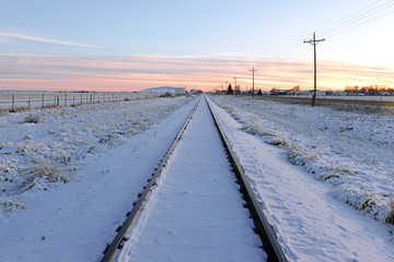 Fototapeta na wymiar Snow covered Train tracks into the horizon at sunset