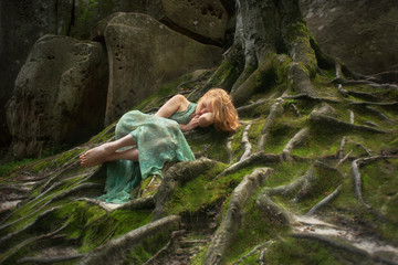 Freckles, red-haired woman in fairy forest on the moss and tree roots