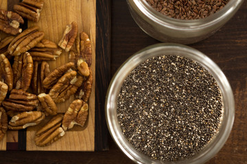 Chia seeds in container beside cutting board, pecans, flax seeds