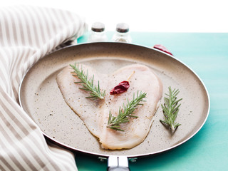 Heart shaped raw chicken breast with herb rosemary and red pepper in skillet. Healthy diet home made dinner on green pastel background