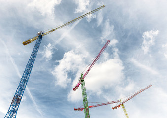 Looking up at three colourful cranes at a blue sky