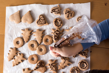 Kid making decoration on gingerbread cookie close up. Baking wit