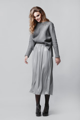 Studio portrait of a full-length stylish young girl in a gray skirt and a gray sweater on a gray...