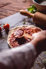 Girl is placing tomato sauce on fresh pizza