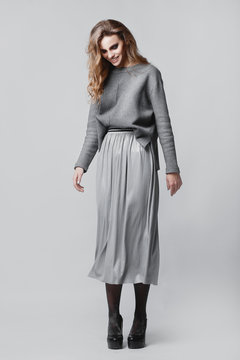 Studio portrait of a full-length stylish young girl in a gray skirt and a gray sweater on a gray background
