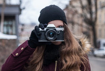 Hipster girl photographer with retro camera taking photo on city street