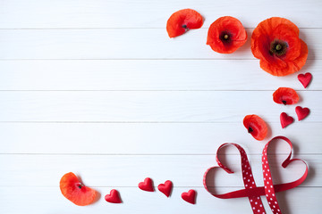 Wooden background with poppies, red hearts, ribbon