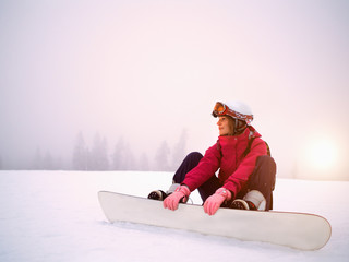 Attractive female sportsman sitting in snow in winter costume on  mountain. Winter landscape in background.