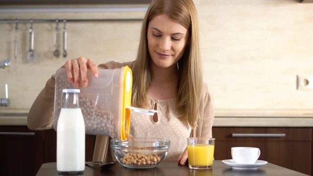 Beautiful young attractive woman pouring cornflakes in a bowl for breakfast in the kitchen.