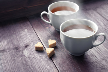 Cups of tea with brown sugar heart shape on wooden background. 