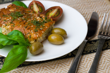 Slice of a cabbage pie, olives, tomatoes, basil on the white pla