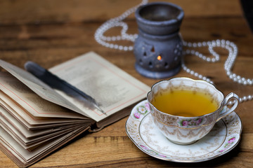 open old book on the wooden desk, porcelain cup of tea and sauce