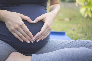 Close up of pregnant woman holding hands with heart shaped in garden