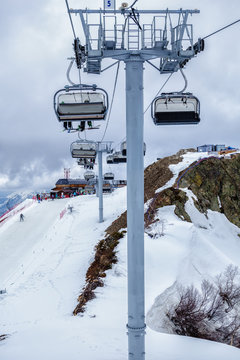 Skiers and snowboarders being transported on a chair ski lift in Sochi mountain ski resort on a cloudy winter day. Vertical landscape