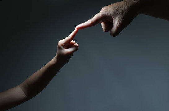 two hands, father and kid, touch each other as symbol of family love and trust on black background