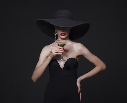 Luxury woman in a large black hat and bright lips with a glass of Martini.