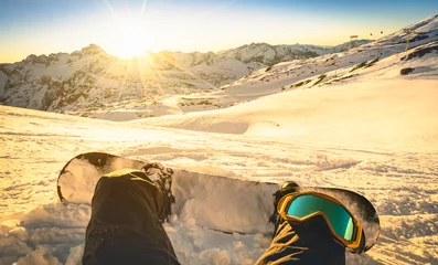 Crédence de cuisine en verre imprimé Sports dhiver Snowboarder sitting on relax moment at sunset in french alps ski resort - Winter sport concept with person on top of the mountain ready to ride down - Legs view point with warm backlighting filter