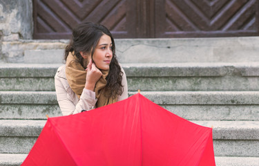 Pensive young woman with red umbrella sitting on the stairs in the old town.
