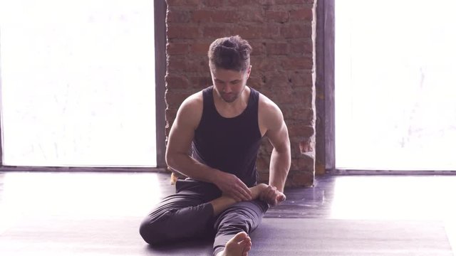 Portrait of a handsome man practicing meditation and yoga against an urban background with picture window and red brick wall on black wooden floor