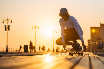 Silhouette of young boy riding longboard on the boardwalk, warm summer time sunset