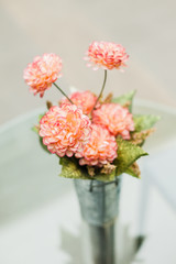 artificial red flowers made from cloth with steel jug ont the glass table 