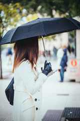 Modern and Elegant woman with umbrella at the city, using mobile