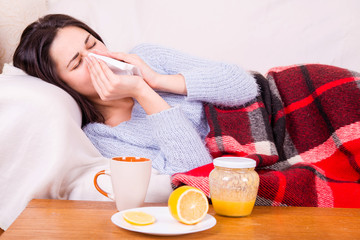 Girl with cold lying under a blanket holding a tissue