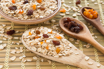 Oat flakes with apricots pieces and raisins in the wooden spoons and in the dish on the table in the kitchen. Healthy eating and lifestyle.