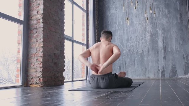 Portrait of a handsome man practicing meditation and yoga against an urban background with picture window and red brick wall on black wooden floor