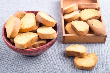 Pieces of rusk in the old brown wooden bowl on a gray tablecloth