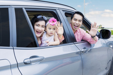 Cheerful family waving hands in the car